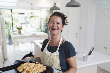 Porträt einer glücklichen Frau mit frischem hausgemachtem Apfelkuchen in der Küche - CAIF29585