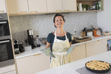 Porträt glückliche Frau mit hausgemachtem Bratapfelkuchen in der Küche - CAIF29591