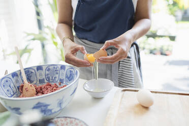 Woman cracking egg over bowl in kitchen - CAIF29593