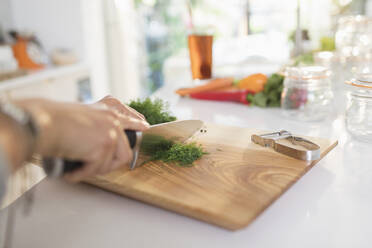 Woman cutting fresh dill on cutting board - CAIF29597