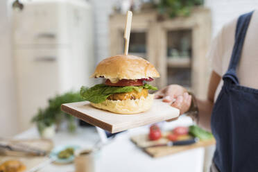 Close up woman holding cheeseburger on cutting board - CAIF29614