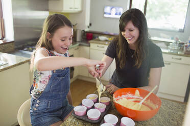 Glückliche Mutter und Tochter backen Muffins in der Küche - CAIF29630