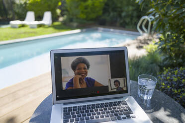 Women video conferencing on laptop screen at sunny poolside - CAIF29662