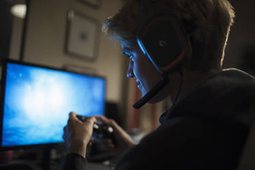 Teenage boy with headset playing video game at computer in dark room - CAIF29665
