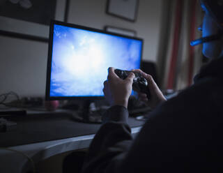 Teenage boy playing video game at computer in dark bedroom - CAIF29670