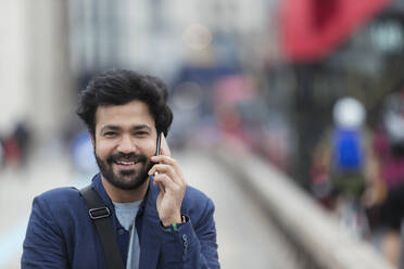 Porträt lächelnder Geschäftsmann im Gespräch mit Smartphone im Freien - CAIF29682