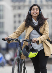 Smiling woman with headphones walking bicycle - CAIF29683