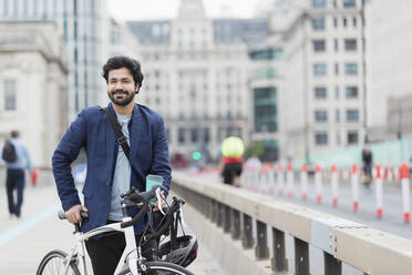 Portrait smiling businessman with bicycle and coffee on city bridge - CAIF29686