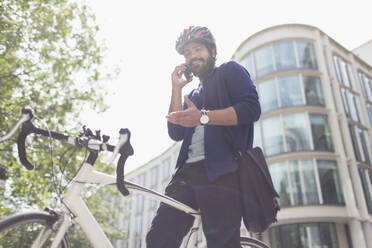 Geschäftsmann mit Fahrrad, der in einer sonnigen Stadt mit seinem Smartphone telefoniert - CAIF29709