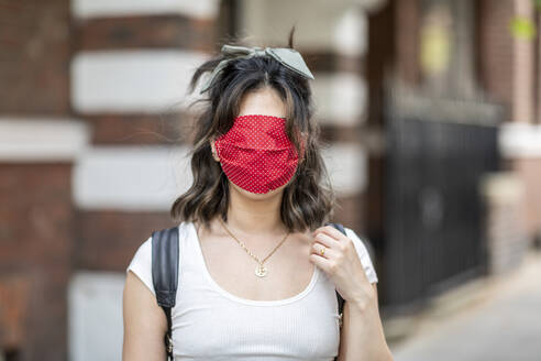 Close-up of woman's face covered with red mask standing against building in city - WPEF03343
