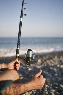 Close-up of mid adult man holding fishing rod at beach against