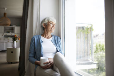 Senior woman looking out of window while sitting at home - RBF07785