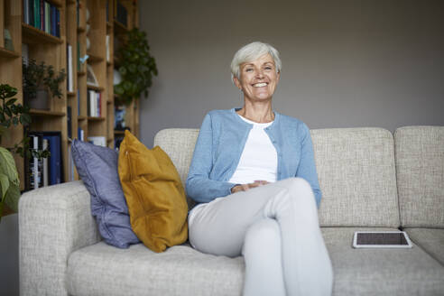 Lächelnde ältere Frau sitzt zu Hause auf dem Sofa - RBF07800