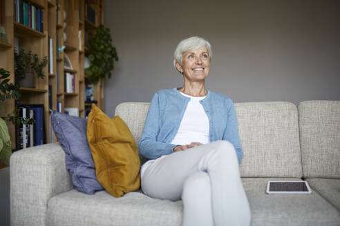 Lächelnde Frau, die wegschaut, während sie zu Hause sitzt - RBF07801