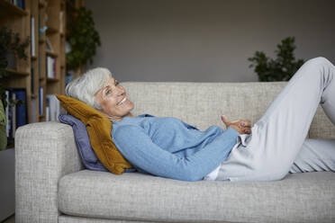 Smiling senior woman lying down on sofa at home - RBF07802