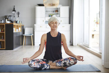 Active senior woman meditating on exercise mat at home - RBF07805