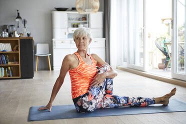 Aktive ältere Frau macht Yoga auf einer Übungsmatte sitzend zu Hause - RBF07806