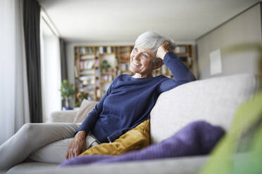 Lächelnde ältere Frau mit dem Kopf in der Hand auf dem Sofa zu Hause sitzend - RBF07809