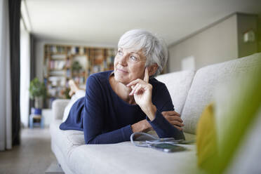 Contemplating senior woman looking away while lying on sofa at home - RBF07818