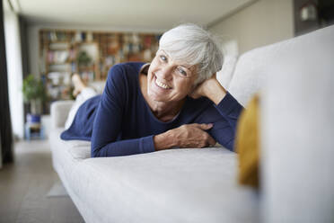 Lächelnde ältere Frau mit dem Kopf in der Hand auf dem Sofa zu Hause liegend - RBF07819