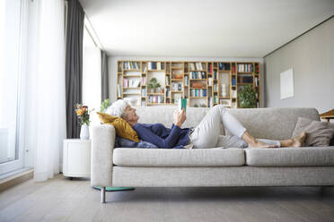 Ältere Frau liest einen Brief, während sie zu Hause auf dem Sofa liegt - RBF07828