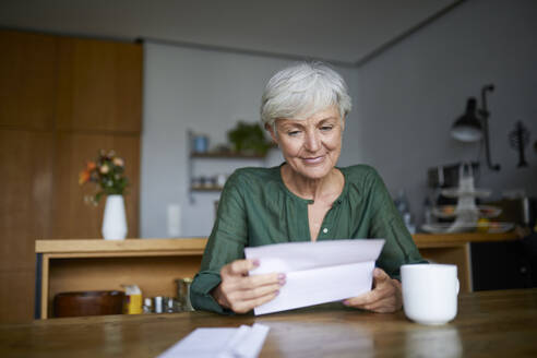 Senior woman reading letter while sitting at home - RBF07832