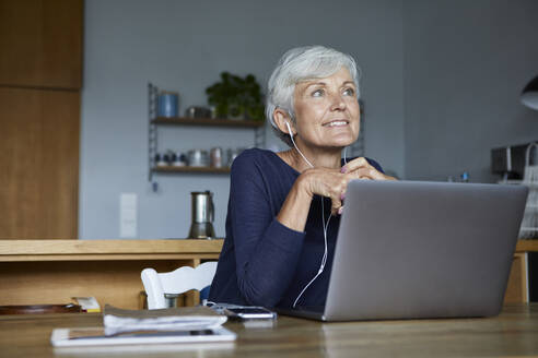 Aktive ältere Frau, die zu Hause mit ihrem Smartphone Musik hört - RBF07851