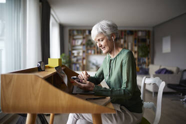 Aktive Senioren hören Musik, während sie zu Hause auf einem Stuhl sitzen - RBF07858