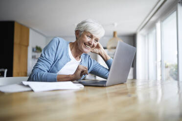 Lächelnde ältere Frau mit Händen hinter dem Kopf, die auf einen Laptop schaut - RBF07866