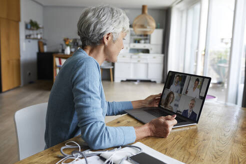 Aktive ältere Frau, die an einer Videokonferenz teilnimmt, während sie zu Hause sitzt - RBF07869