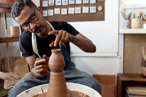 Close-up of male potter making earthenware while sitting in workshop - EGAF00712