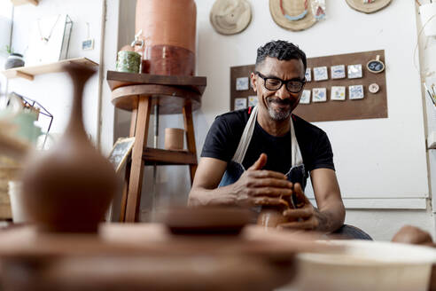 Smiling male artist making pottery in workshop - EGAF00717