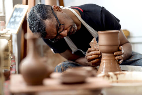Close-up of male artist making earthenware on pottery wheel in workshop - EGAF00719