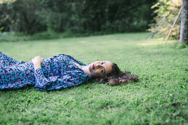 Lächelnde junge Frau auf einer Wiese im Park liegend - DCRF00861