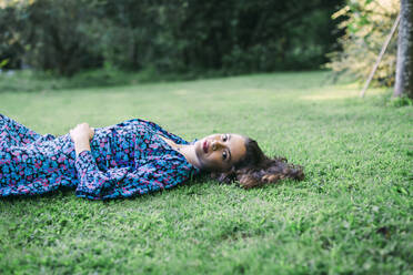 Smiling young woman lying on grassy land in park - DCRF00861