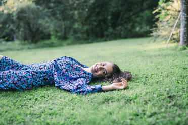 Smiling beautiful woman lying on grassy land in park - DCRF00862