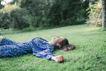 Junge Frau entspannt sich auf einer Wiese vor Pflanzen im Park - DCRF00863