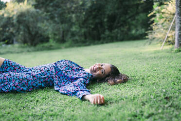 Cheerful young woman resting on grassy land in park - DCRF00864