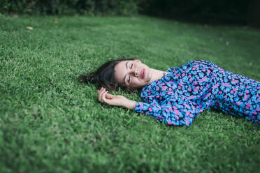 Young woman with eyes closed lying on grassy land in park - DCRF00865