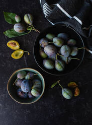 Overhead shot of bowls of fresh plums against a black background. - CAVF88934