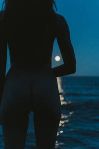 Nackte junge Frau schaut auf das Meer gegen den klaren blauen Himmel in der Nacht - AFVF07271