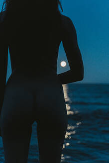 Naked young woman looking at sea against clear blue sky during night - AFVF07271