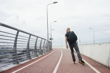 Junger Mann mit Rucksack auf Inline-Skating-Brücke gegen den Himmel - VPIF03033