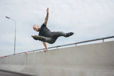 Unbekümmerter junger Mann mit Inline-Skates, der über ein Brückengeländer springt - VPIF03036