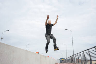 Junger Mann mit Inline-Skates springt auf Brücke gegen Himmel - VPIF03038