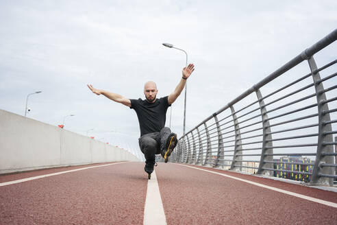 Junger Mann, der einen Stunt beim Inlineskaten auf einer Brücke gegen den Himmel vollführt - VPIF03041