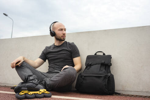 Nachdenklicher junger Mann mit Inline-Skates, der auf einer Brücke sitzend Musik hört - VPIF03050