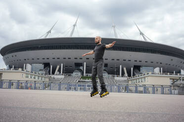 Mann mit ausgestreckten Armen auf Inline-Skates auf der Straße vor einem modernen Gebäude - VPIF03055