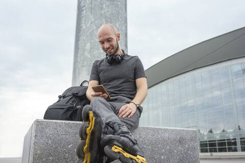 Smiling young man using mobile phone while sitting on seat against sky stock photo