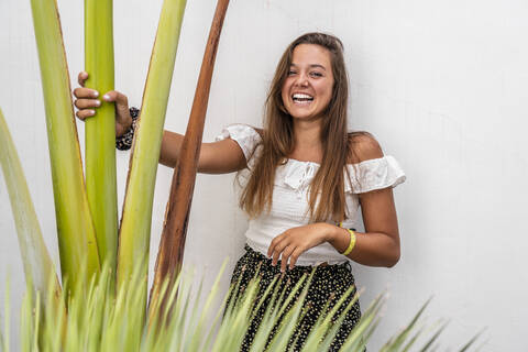 Lächelnde Frau, die eine Pflanze hält und an der Wand steht, lizenzfreies Stockfoto